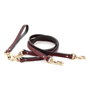 Two-frame slideshow of an Auburn Leathercrafters two-dog walker leash, first isolated on white and then with the handle being held in a man's hand, with grass in the background
